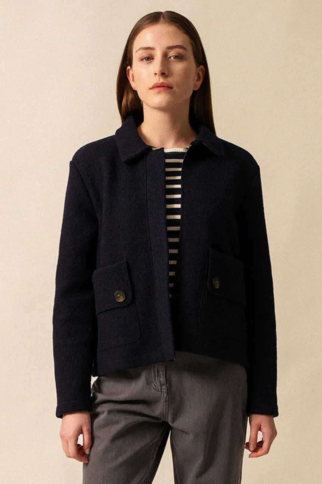Person wearing a navy jacket over a striped shirt on a beige background