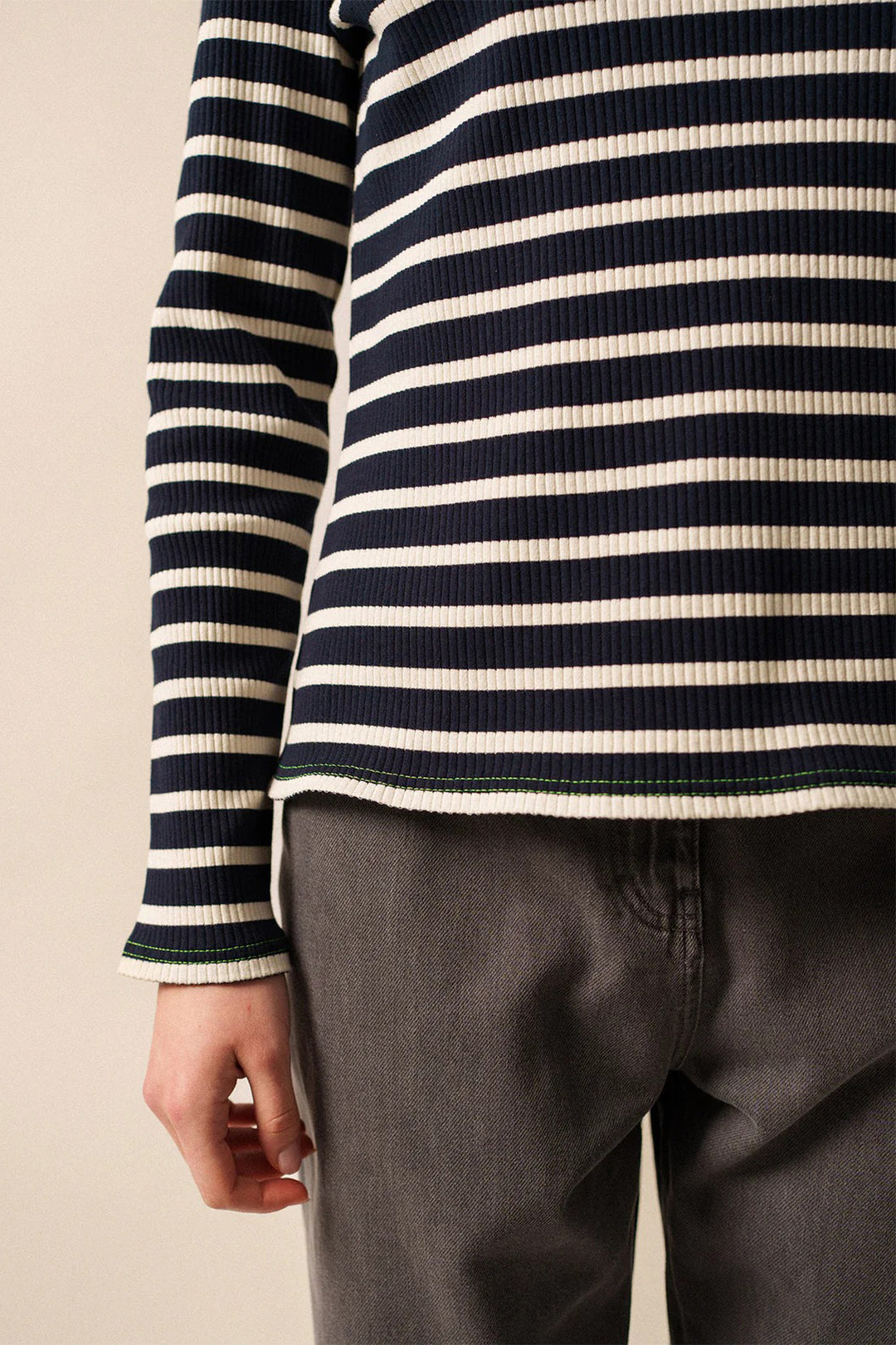 Person wearing a navy and white striped long-sleeve shirt with dark pants on a beige background