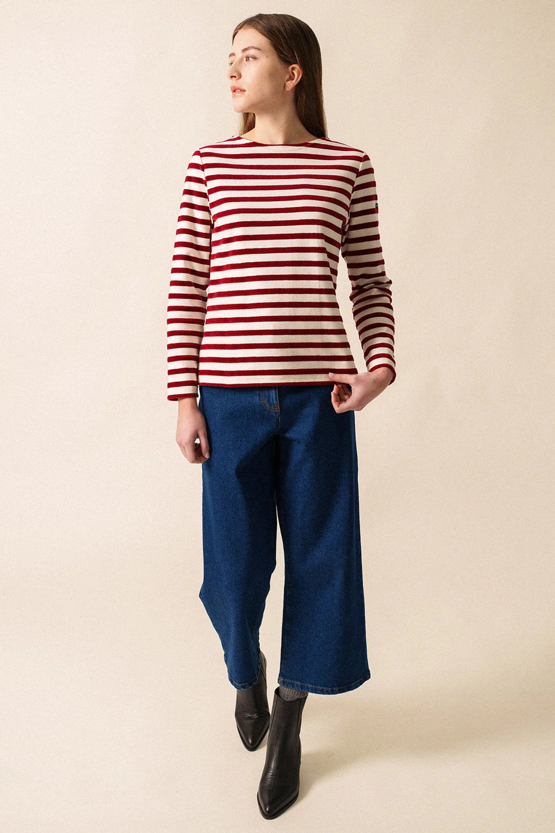 Person wearing a red and white striped sweater with blue jeans on a beige background
