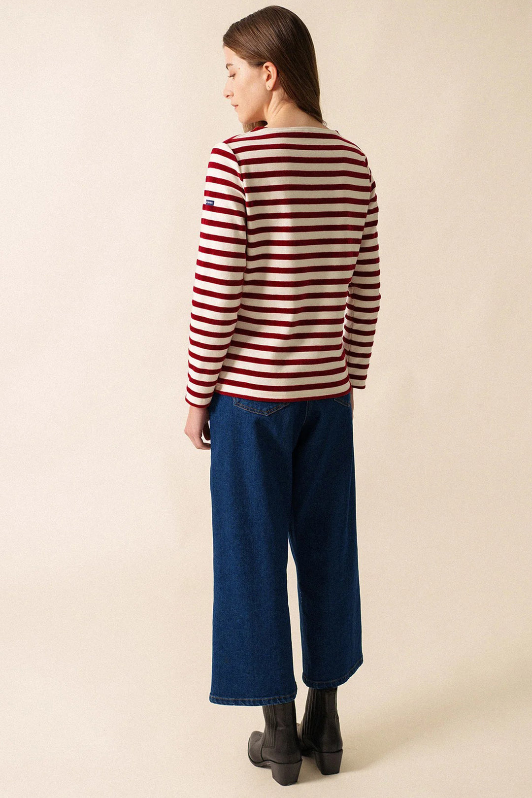 Person wearing a striped sweater and blue jeans on a beige background