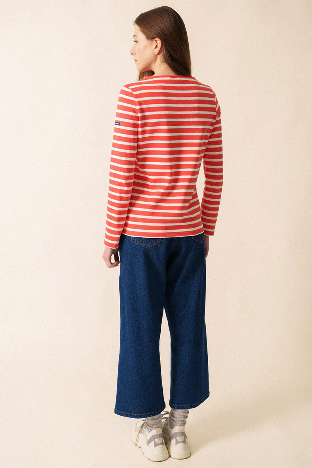 Person wearing a red and white striped shirt and blue jeans on a beige background