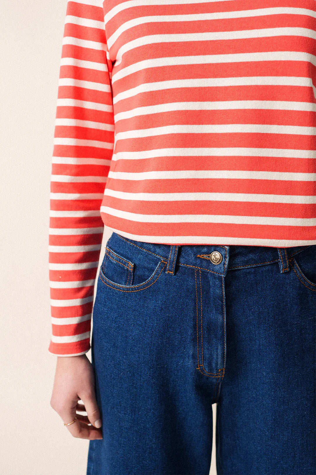 Person wearing a red and white striped shirt with blue jeans on a beige background