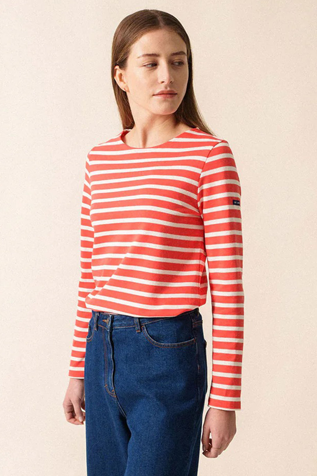 Woman wearing a red and white striped long-sleeve shirt and blue jeans on a beige background