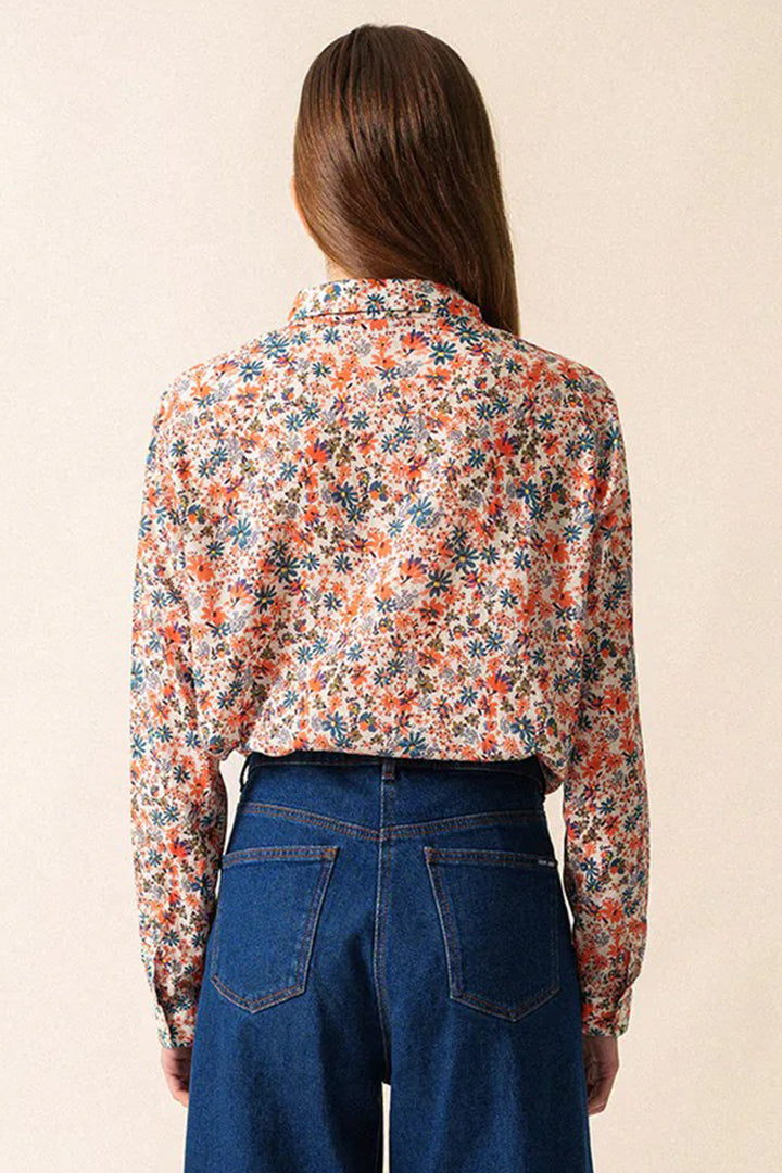 Person wearing a floral blouse and blue jeans on a beige background
