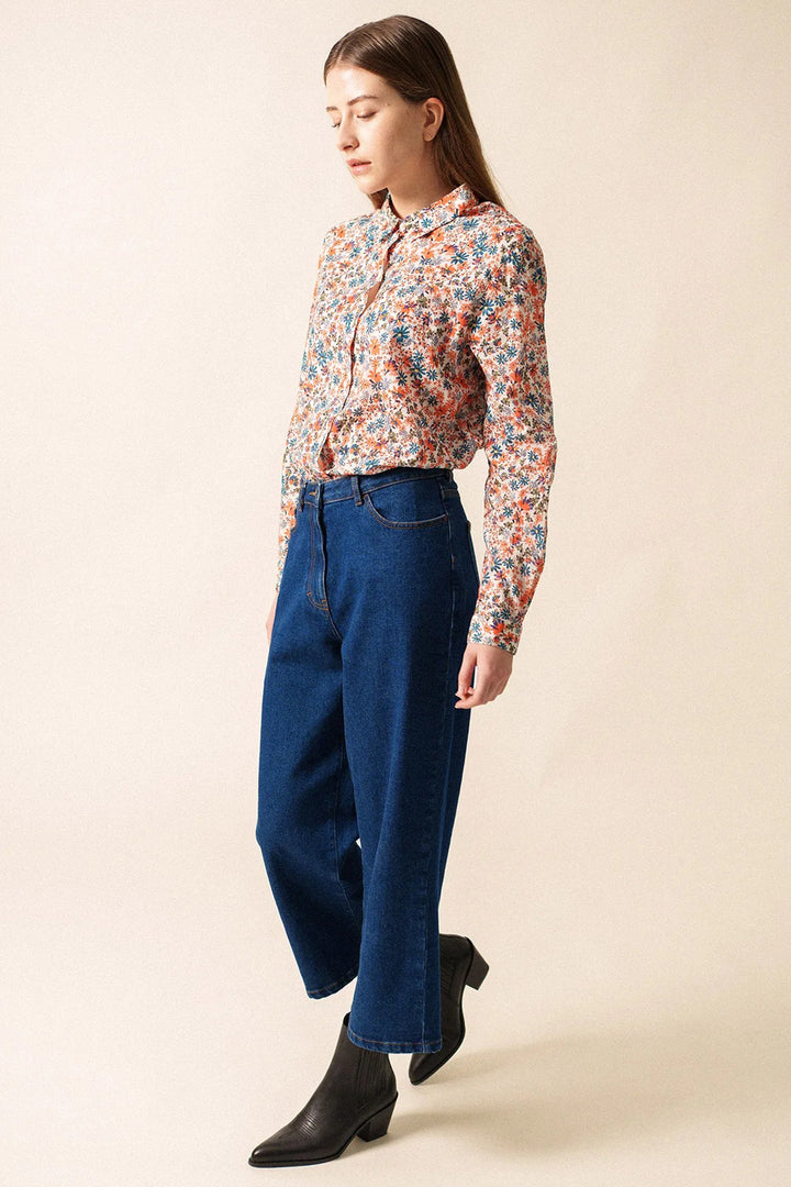 Woman wearing a floral blouse and blue jeans against a beige background
