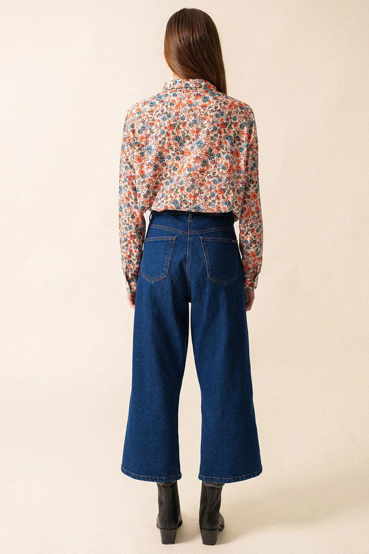 Person wearing a floral blouse and blue jeans on a beige background