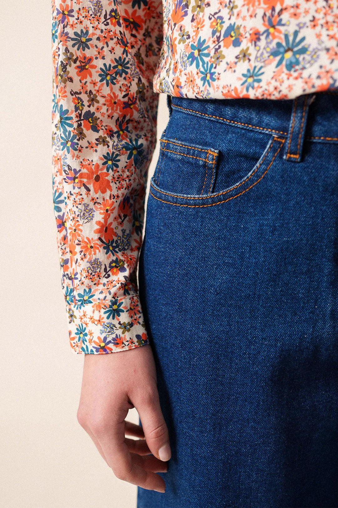 Person wearing a floral long-sleeve shirt and blue denim skirt on a beige background