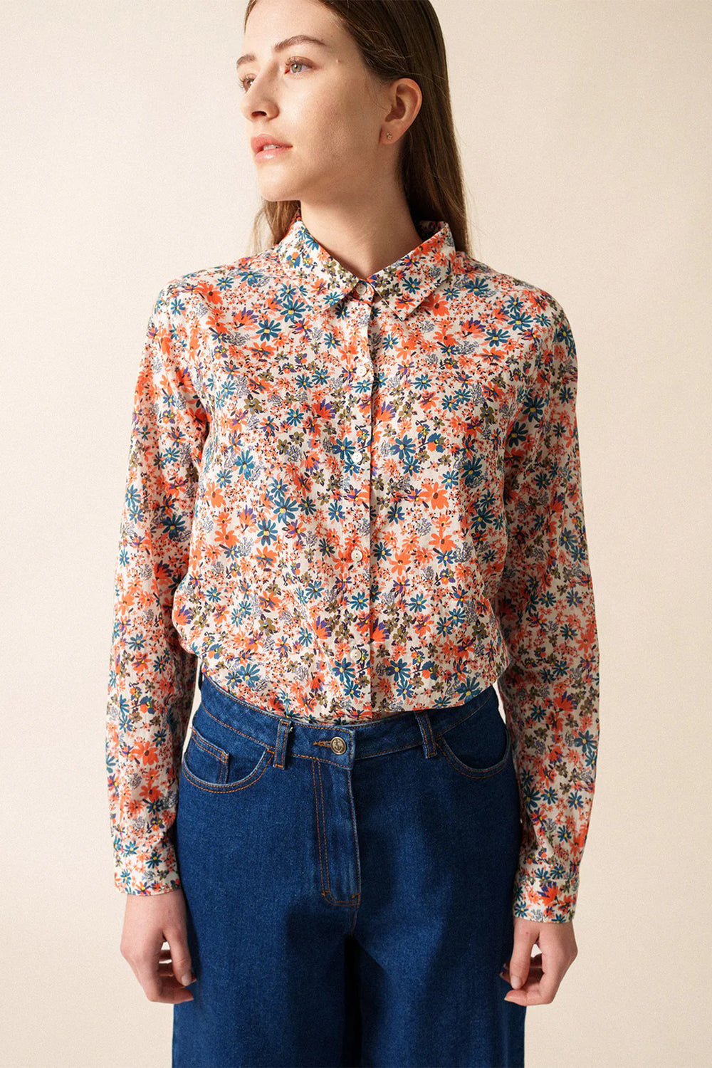 Woman wearing a floral blouse and blue jeans against a beige background