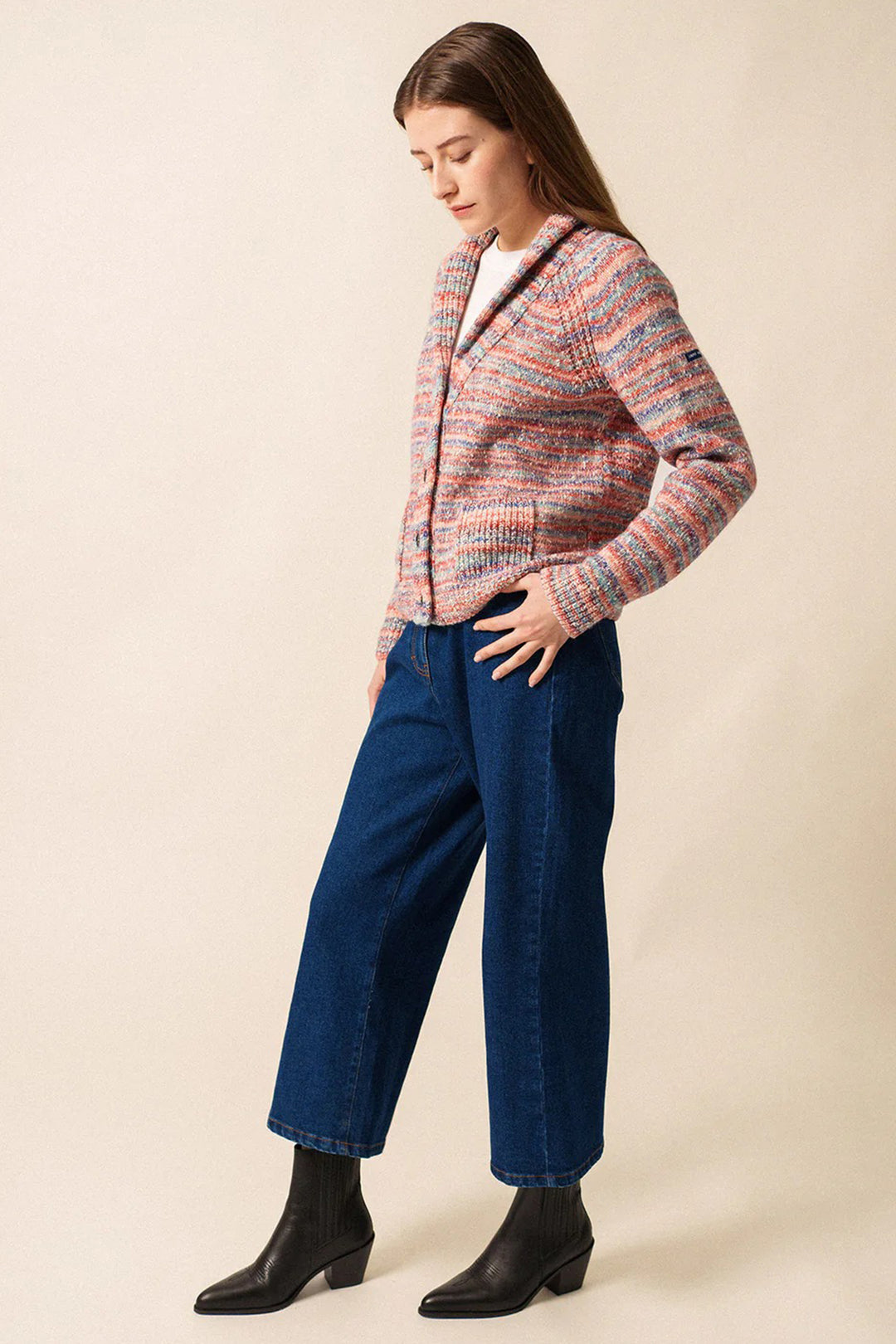 Woman wearing a patterned cardigan and blue jeans against a beige background