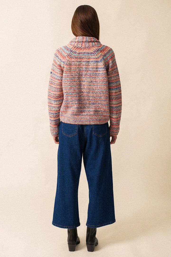 Person wearing a colorful sweater and blue jeans on a beige background
