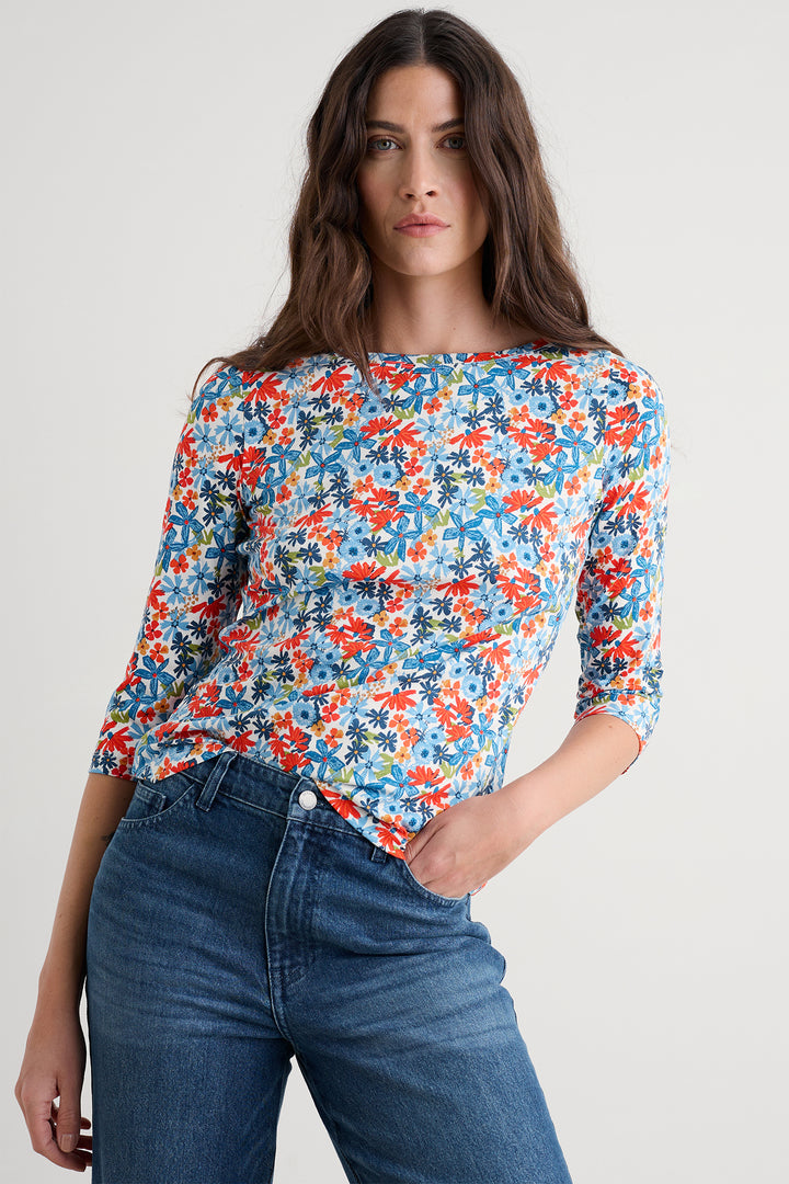 Woman wearing a colorful floral blouse and blue jeans on a plain background
