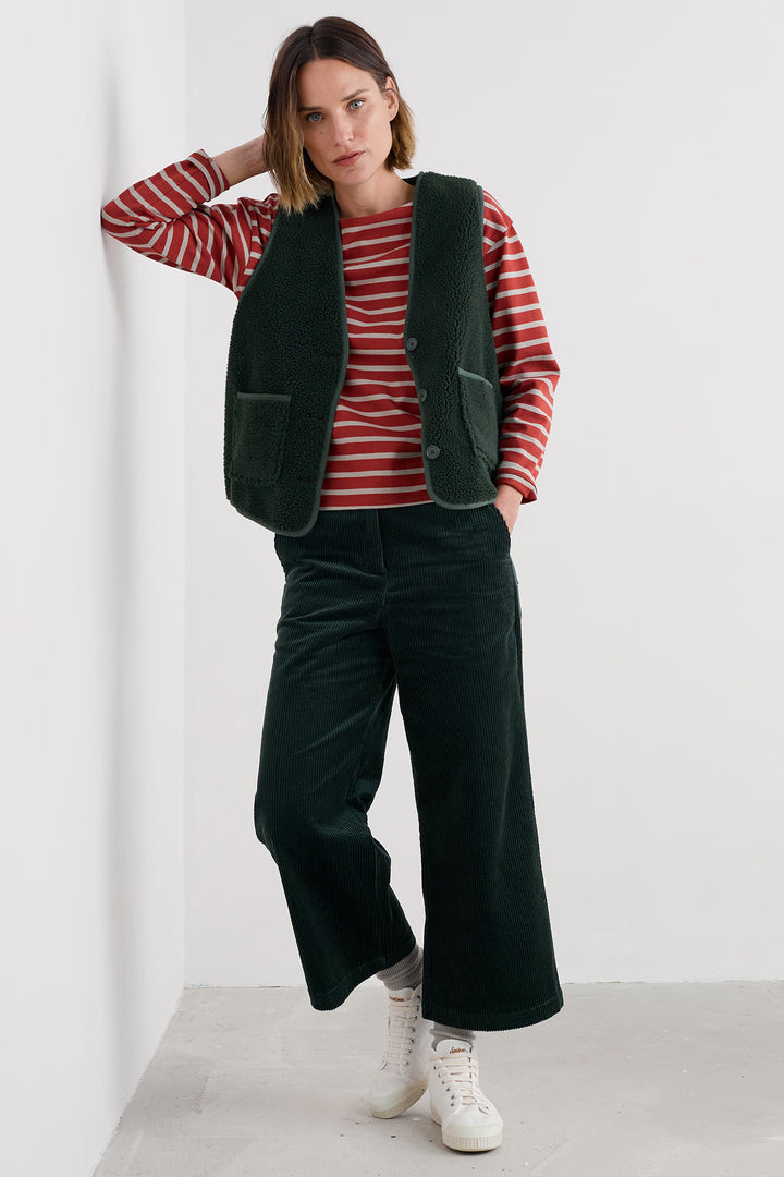 Woman wearing a red striped sweater, green vest, and dark green pants against a white background