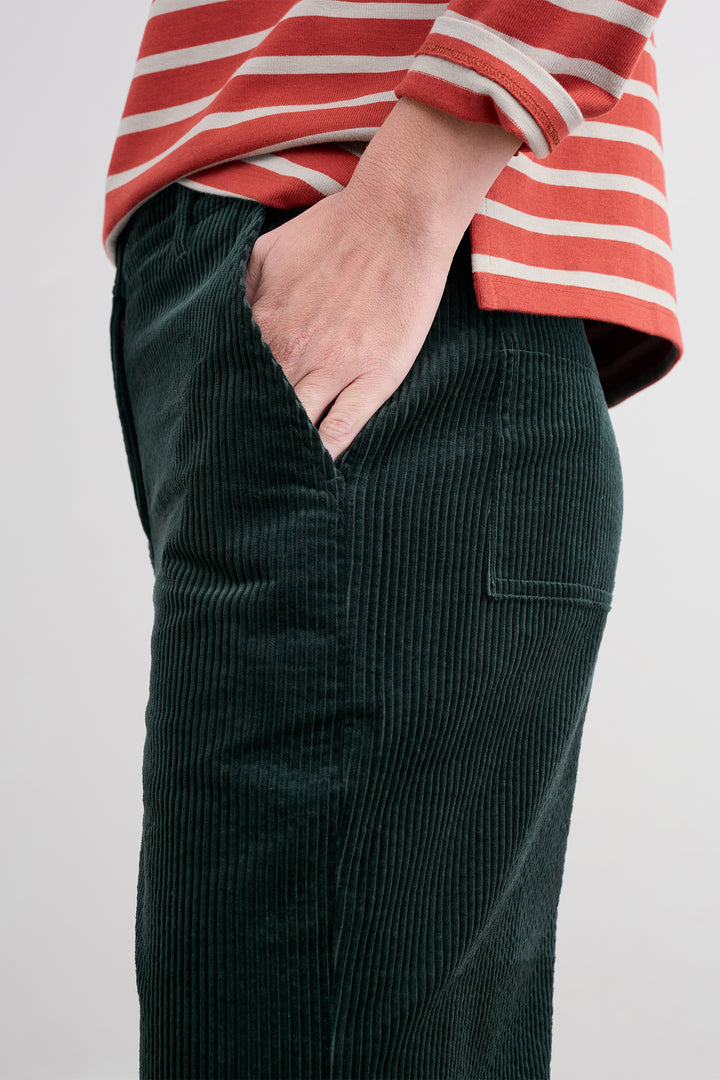 Person wearing a red and white striped shirt with green corduroy pants on a plain background