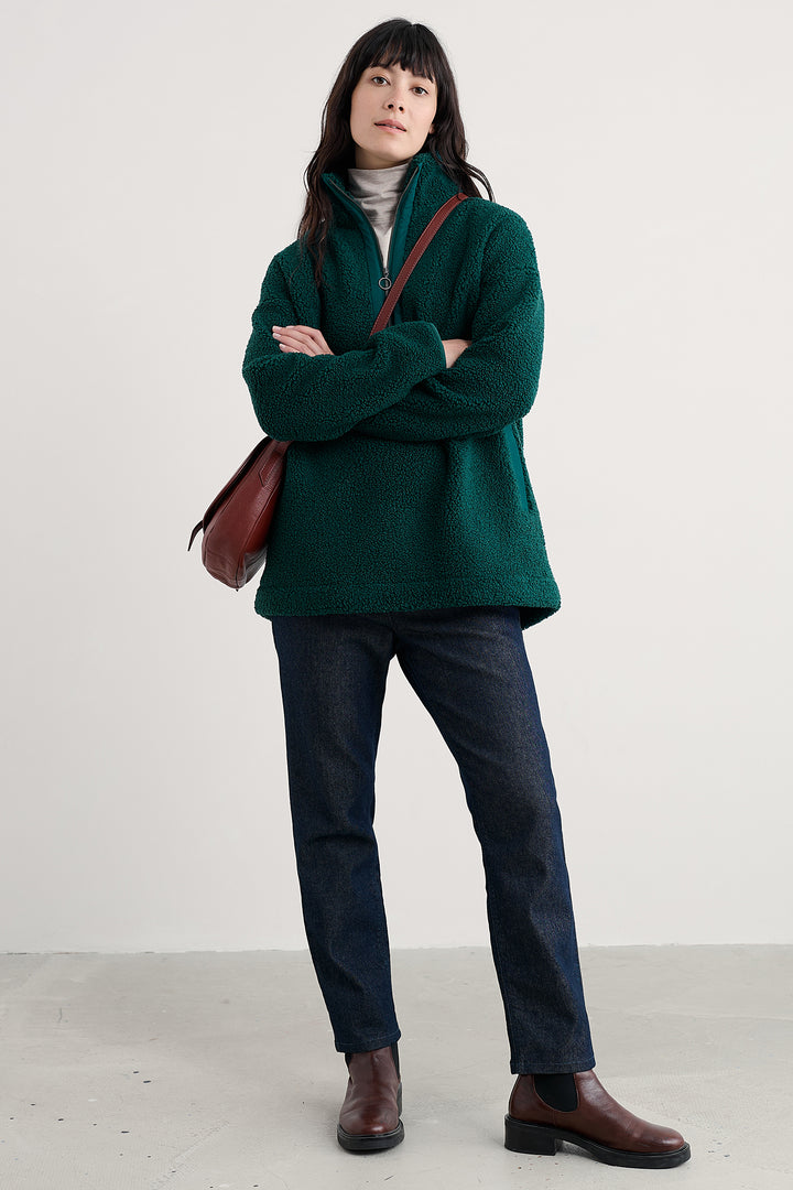 Woman wearing a green sweater and dark pants with a brown leather bag on a white background