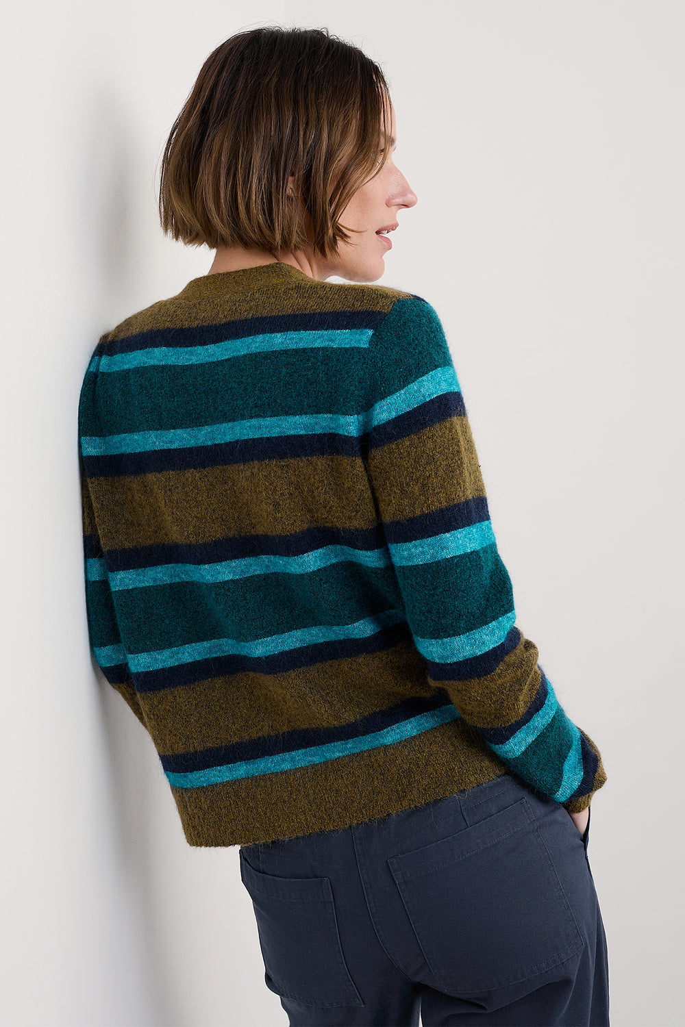 Person wearing a striped sweater with green, blue, and brown colors on a plain background