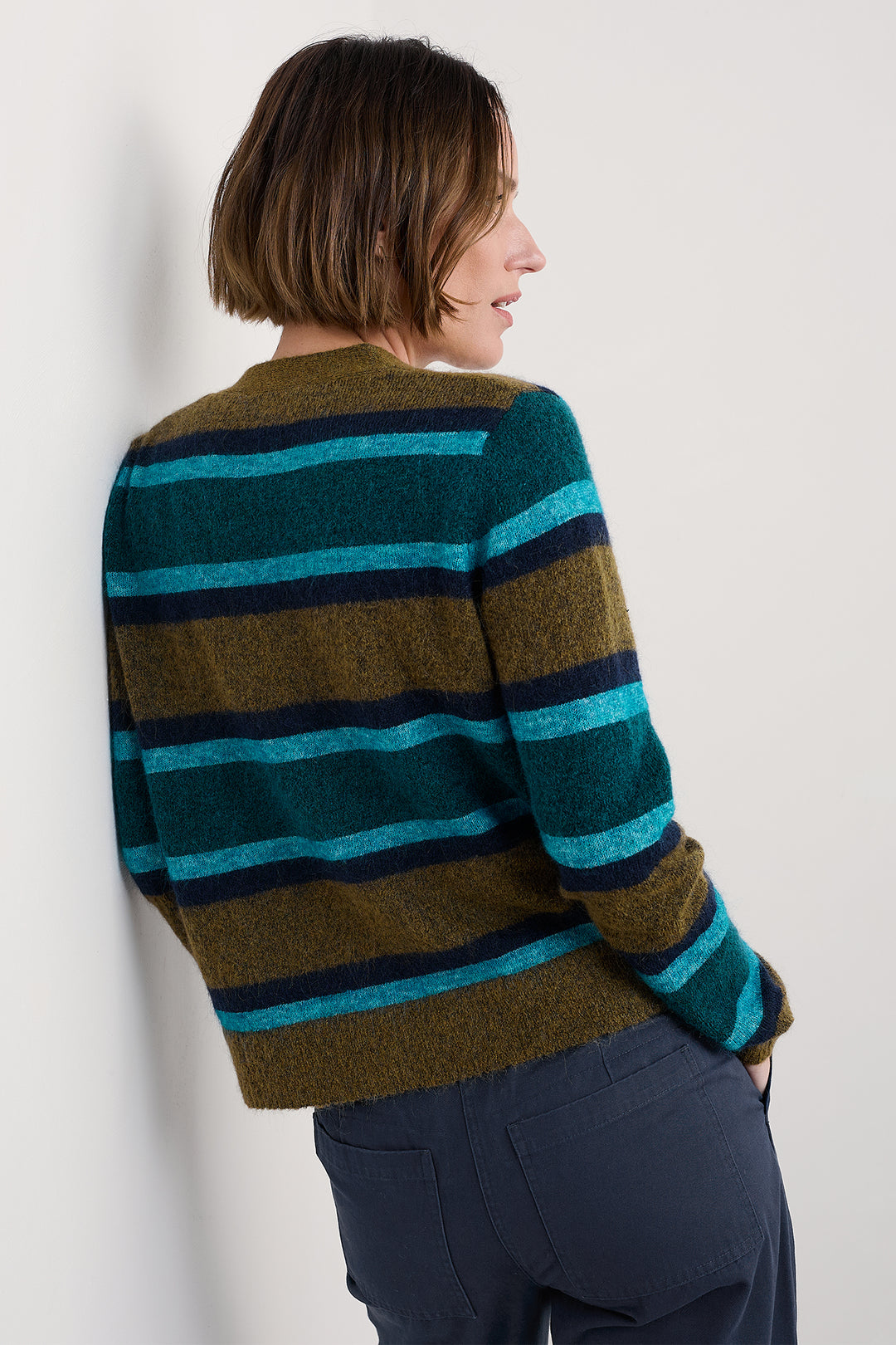 Person wearing a striped sweater with green, blue, and brown colors on a plain background