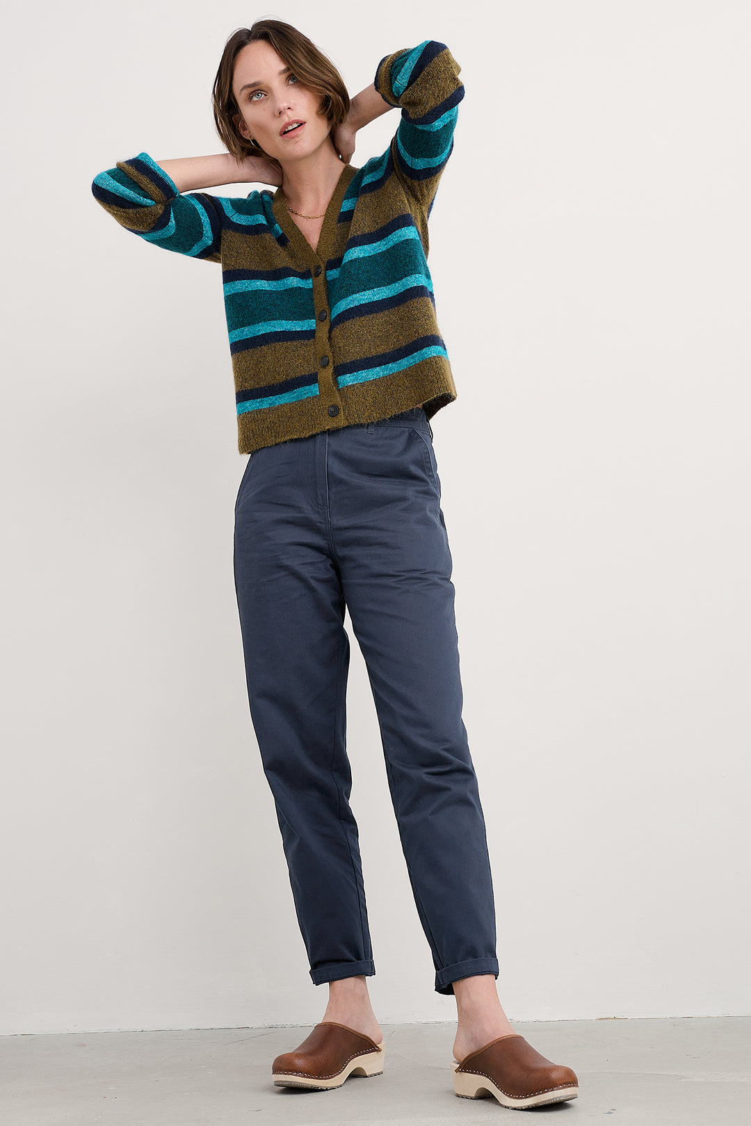 Woman wearing a striped sweater and blue pants against a white background