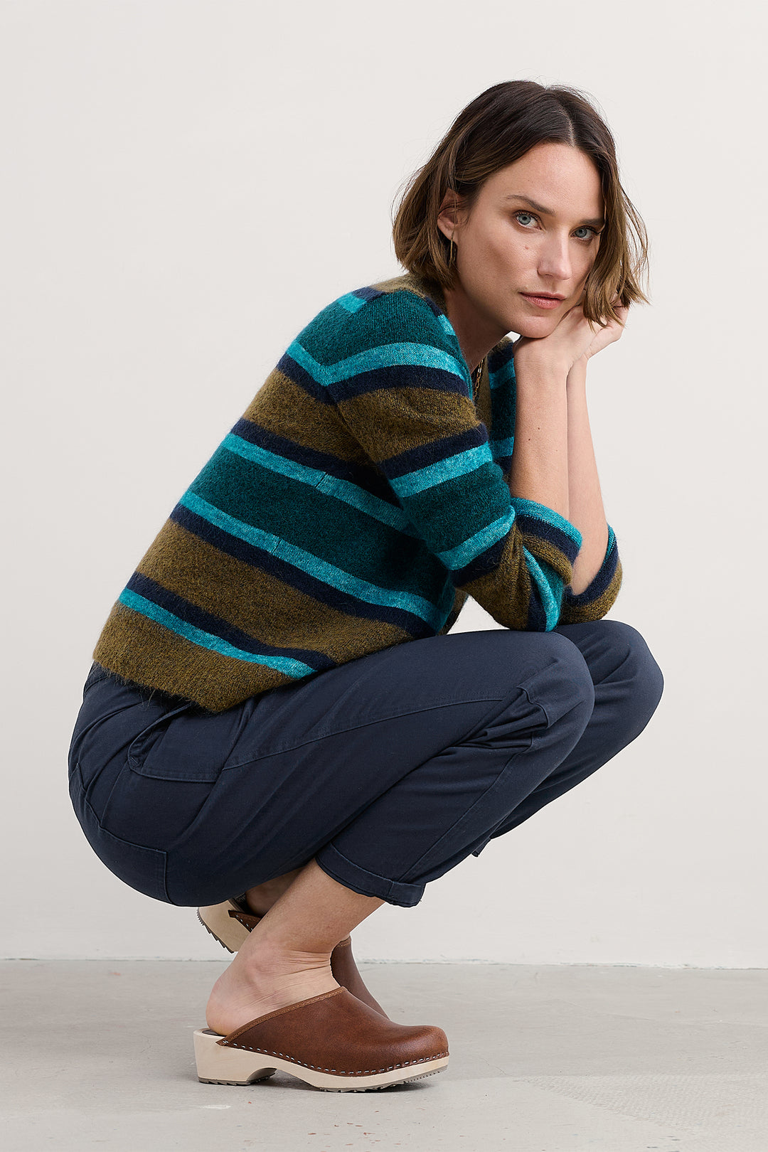 Woman wearing a striped sweater and blue pants, posing on a light background