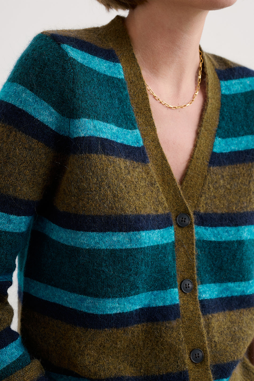 Close-up of a person wearing a striped cardigan with green, blue, and brown colors.