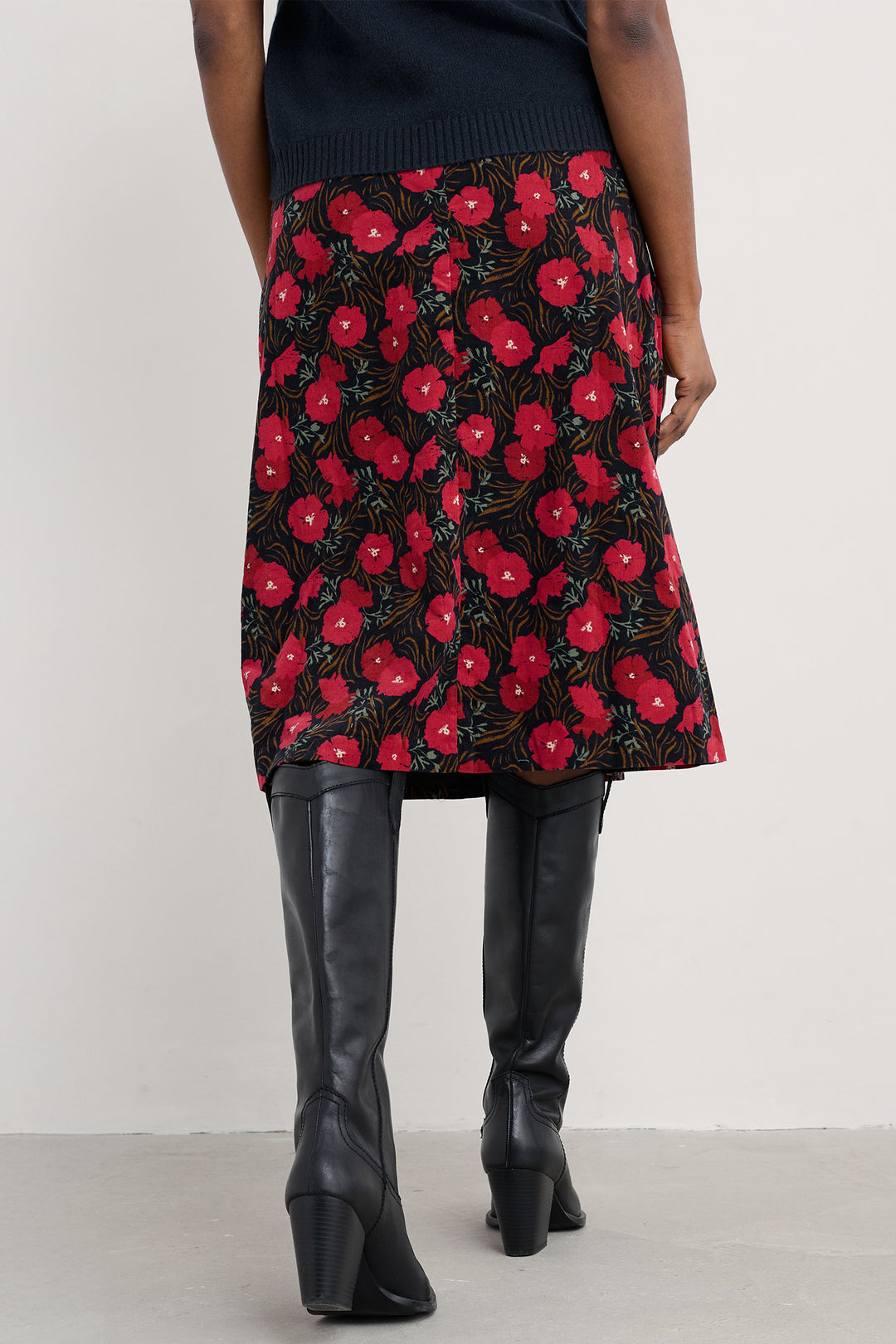 Person wearing a black skirt with red floral pattern and black knee-high boots on a white background