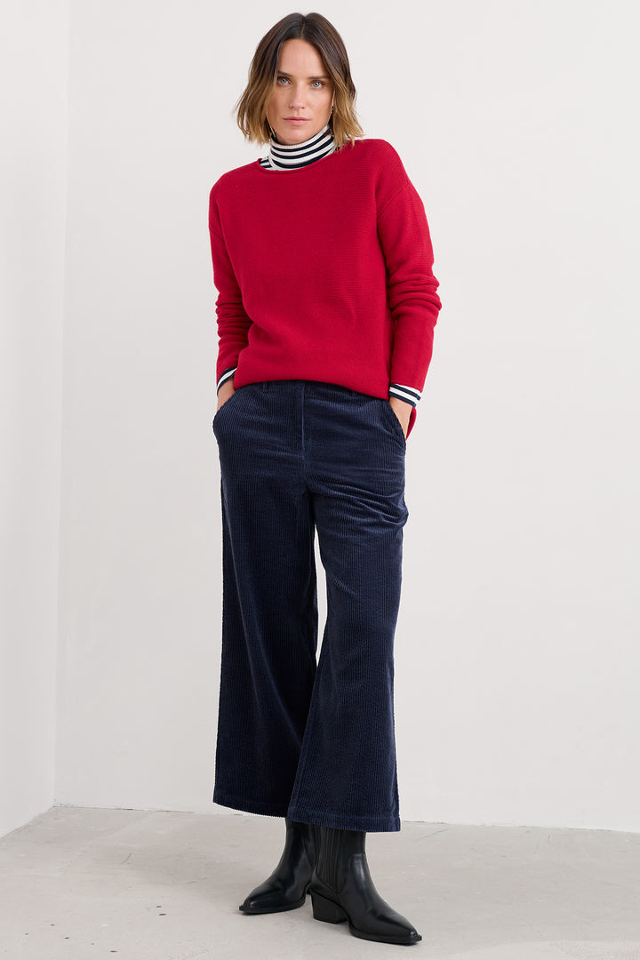 Person wearing a red sweater, navy pants, and black boots on a white background