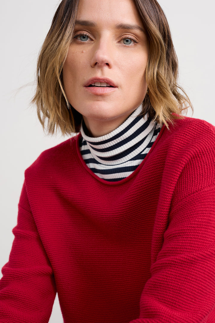 Person wearing a red sweater over a striped turtleneck with a plain background