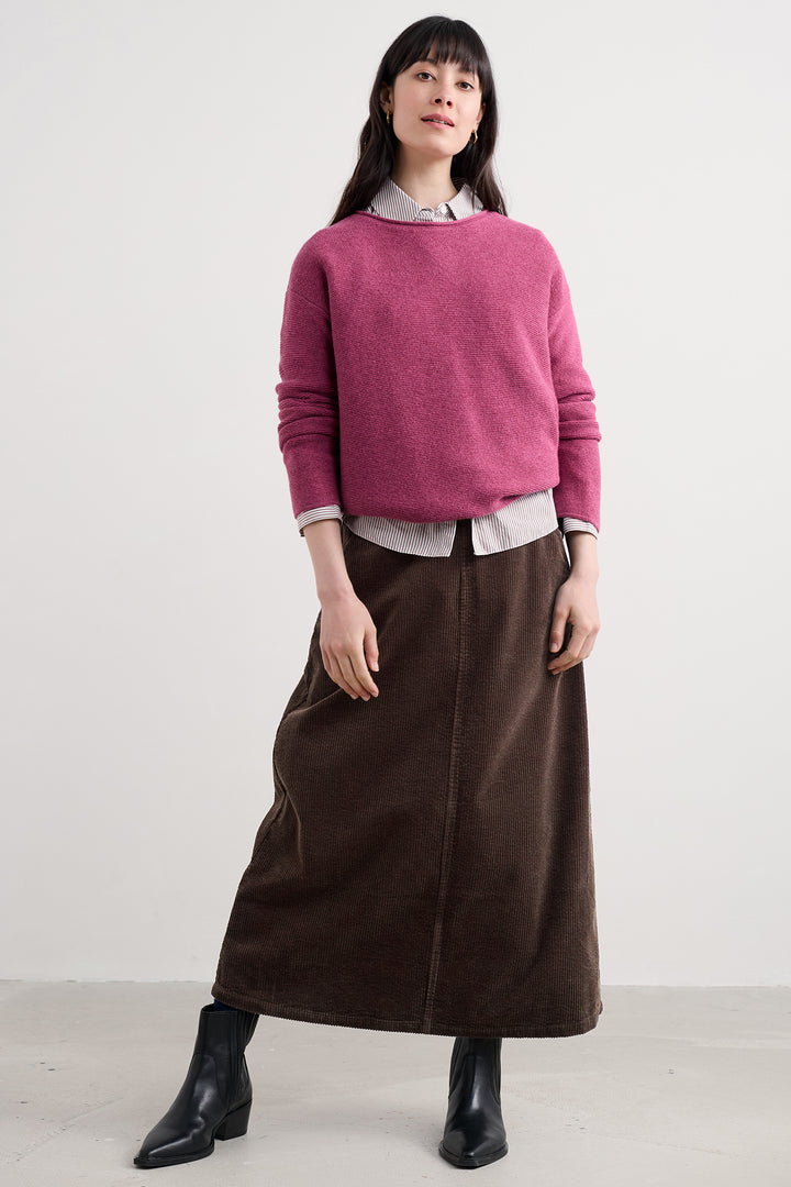 Woman wearing a pink sweater and brown skirt against a white background