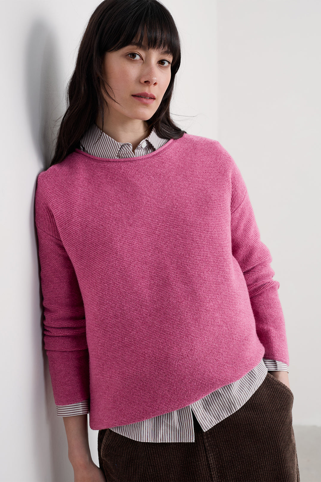 Woman wearing a pink sweater over a striped shirt against a white background