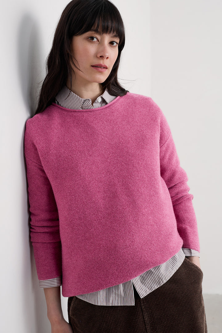 Woman wearing a pink sweater over a striped shirt against a white background