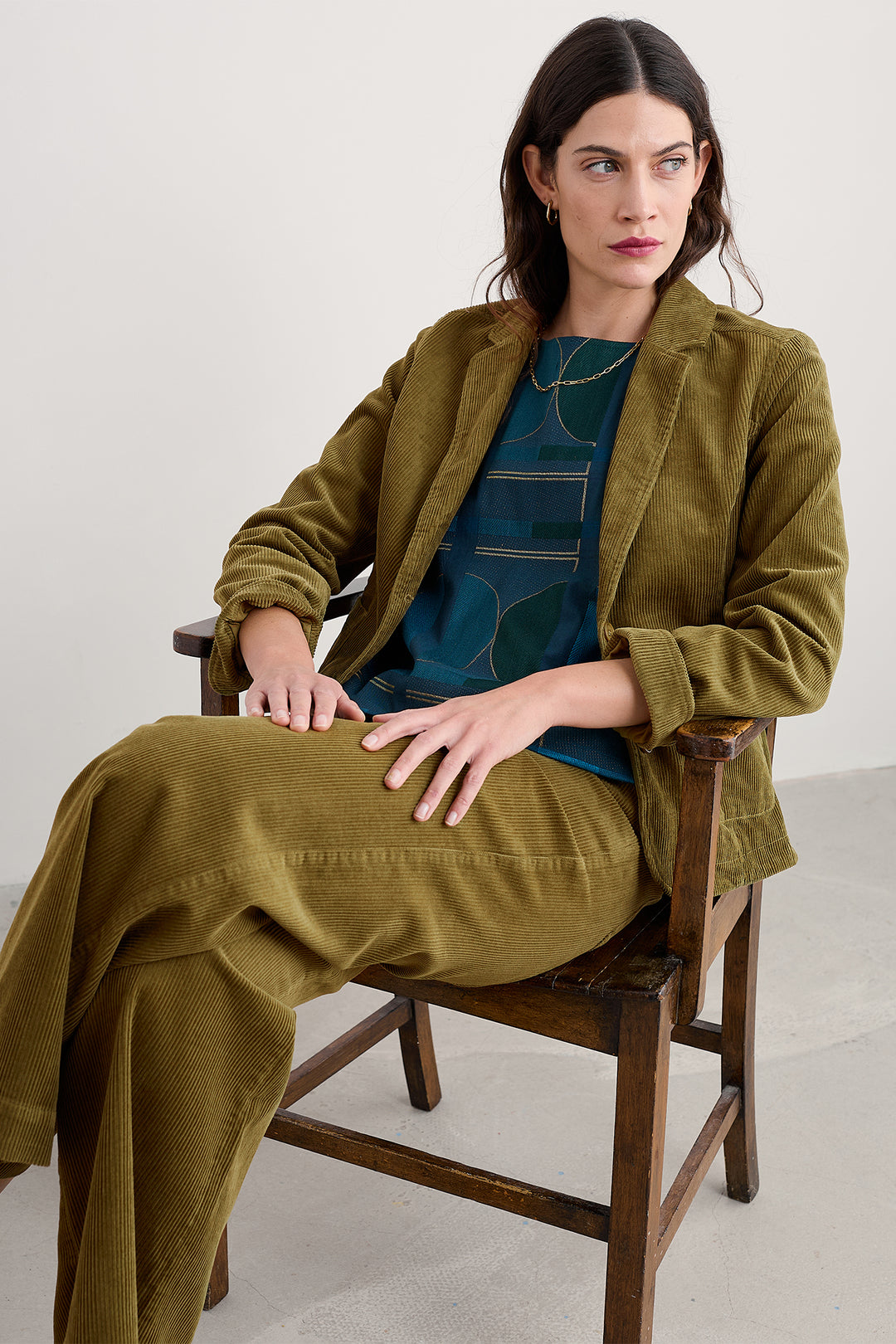 Woman wearing a green coat sitting on a wooden chair against a white background