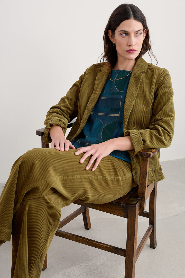 Woman wearing a green coat sitting on a wooden chair against a white background