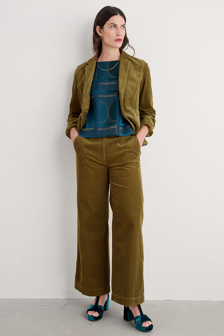 Woman wearing a green jacket and wide-leg pants against a plain background