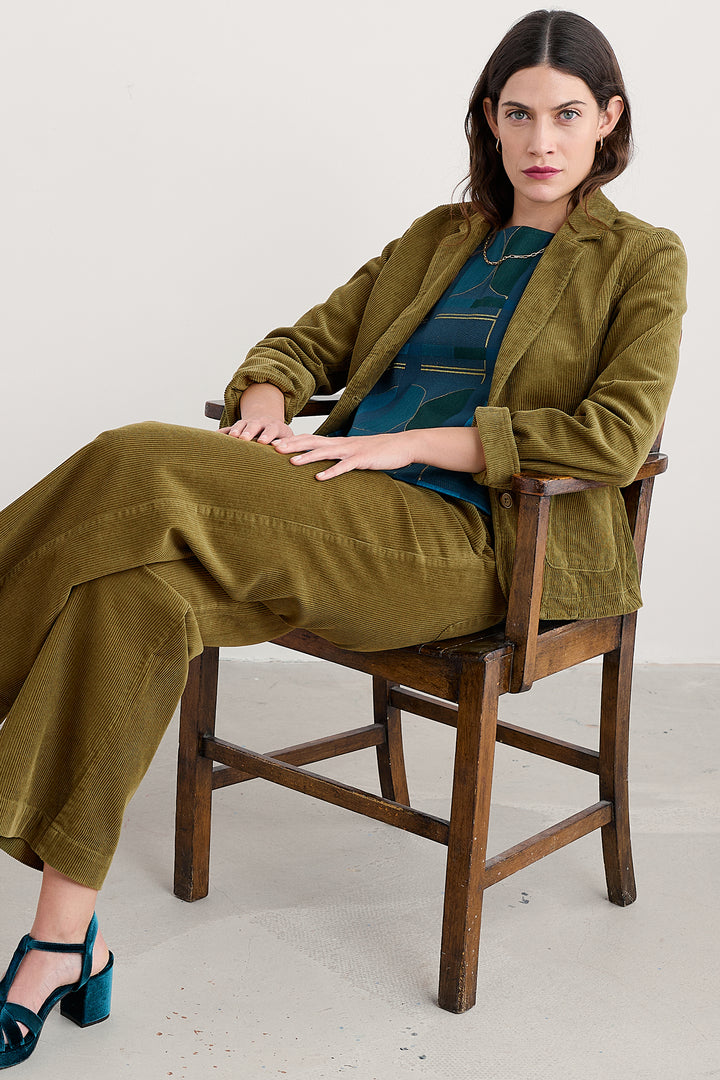Woman in a green outfit sitting on a wooden chair against a white background