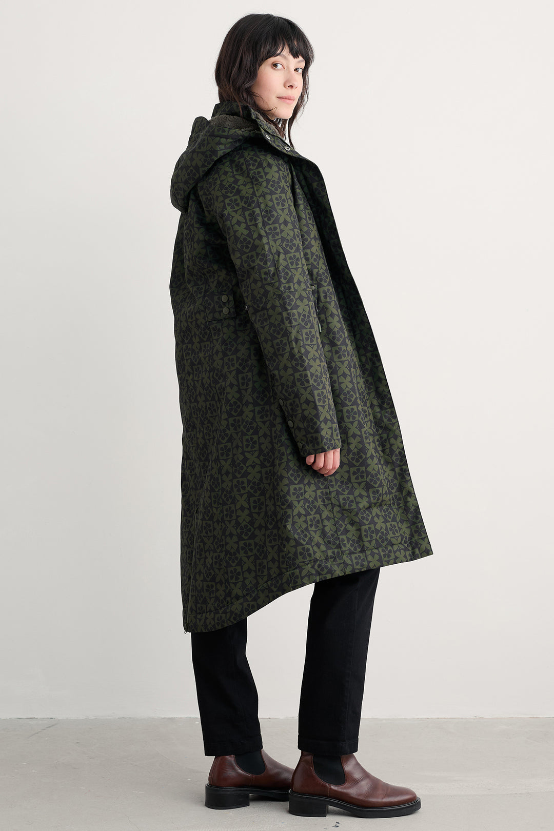 Person wearing a long green coat with a hood on a plain background