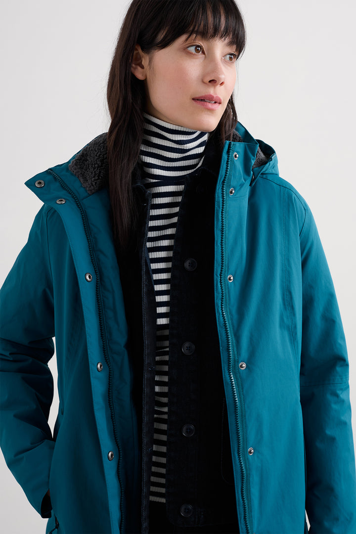 Woman wearing a teal jacket with a striped shirt underneath on a white background
