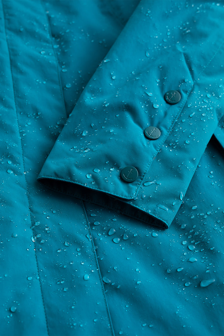 Close-up of a blue raincoat with water droplets on the fabric.