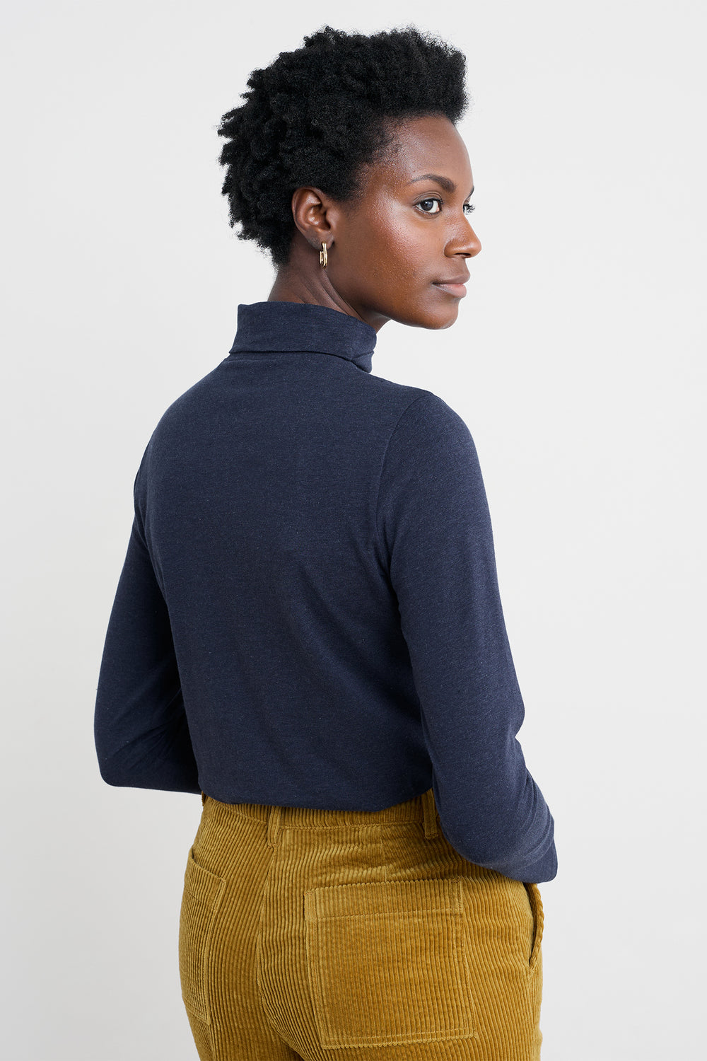 Woman wearing a navy turtleneck and mustard yellow pants on a white background