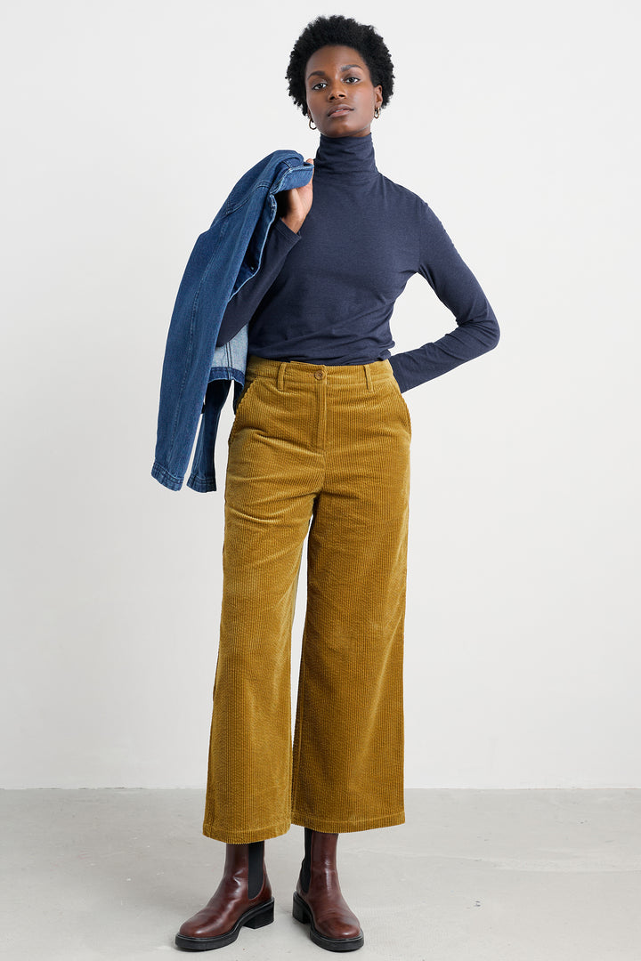 Person wearing a navy turtleneck, mustard yellow pants, and brown shoes on a white background
