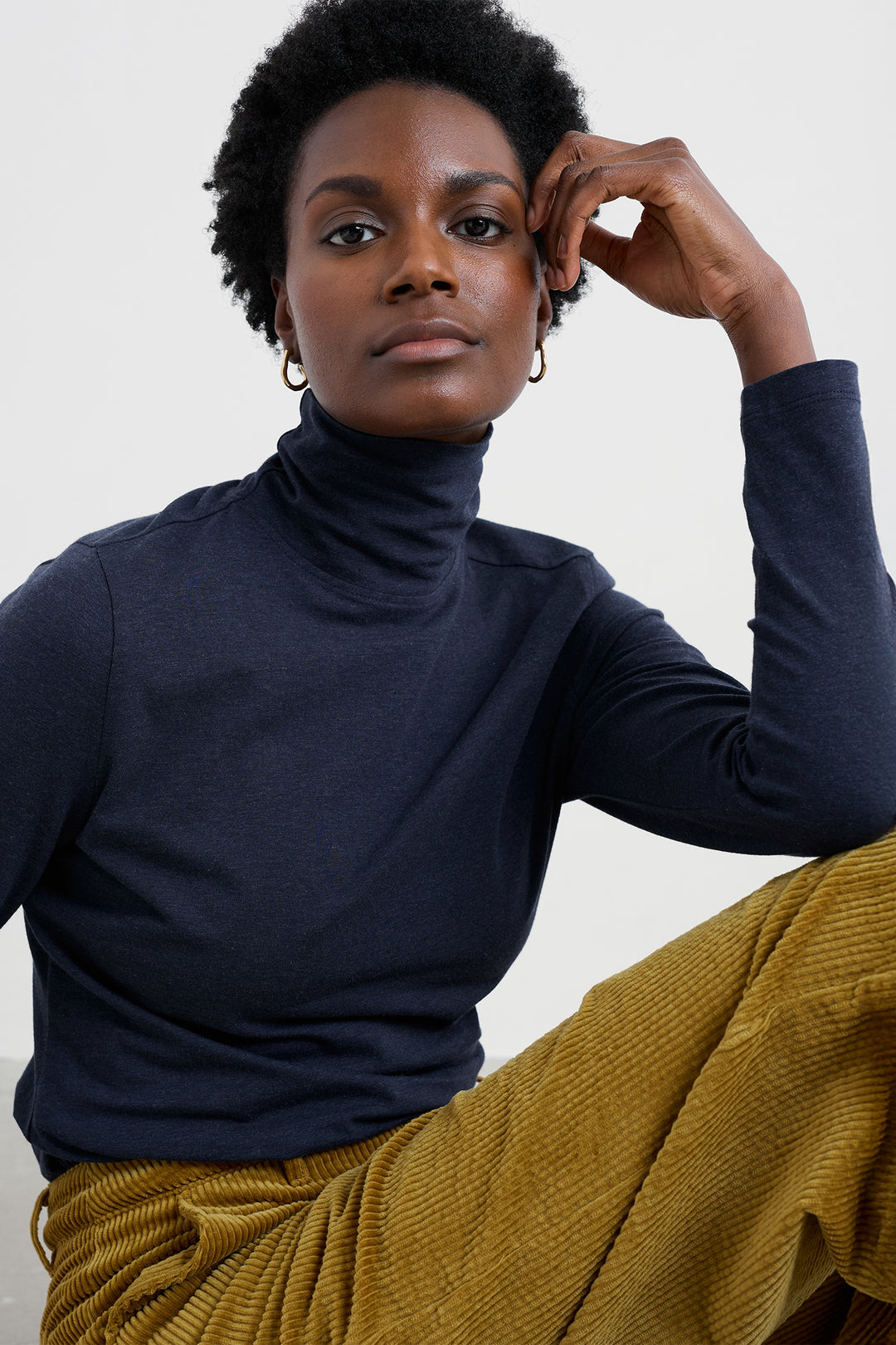 Woman wearing a navy turtleneck and mustard pants against a plain background