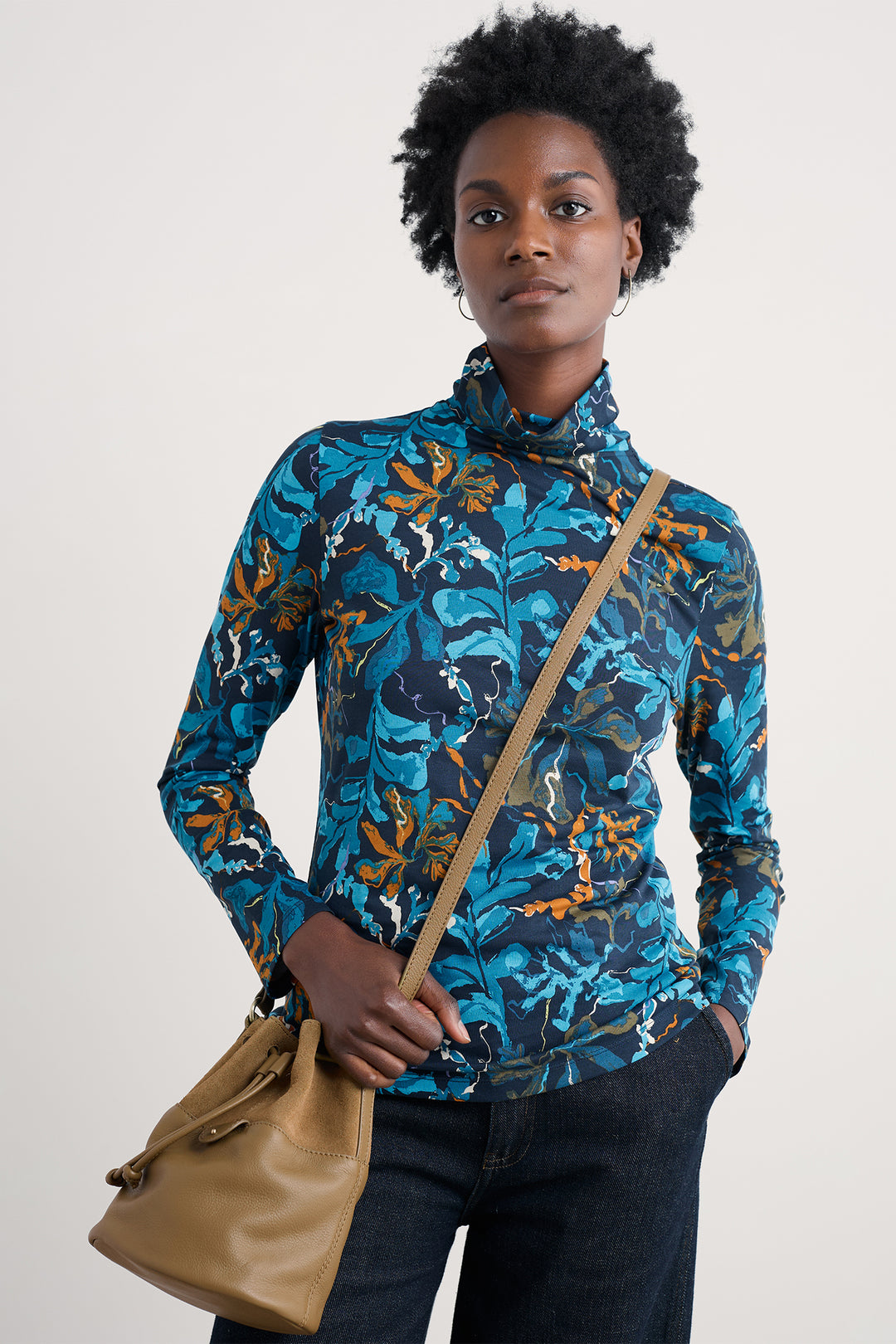 Woman wearing a blue floral patterned jacket holding a brown bag against a white background