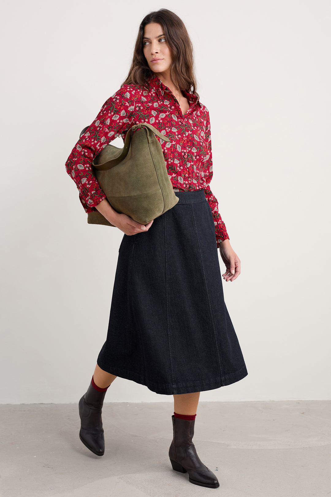 Woman holding a green bag, wearing a red floral blouse and black skirt, on a white background