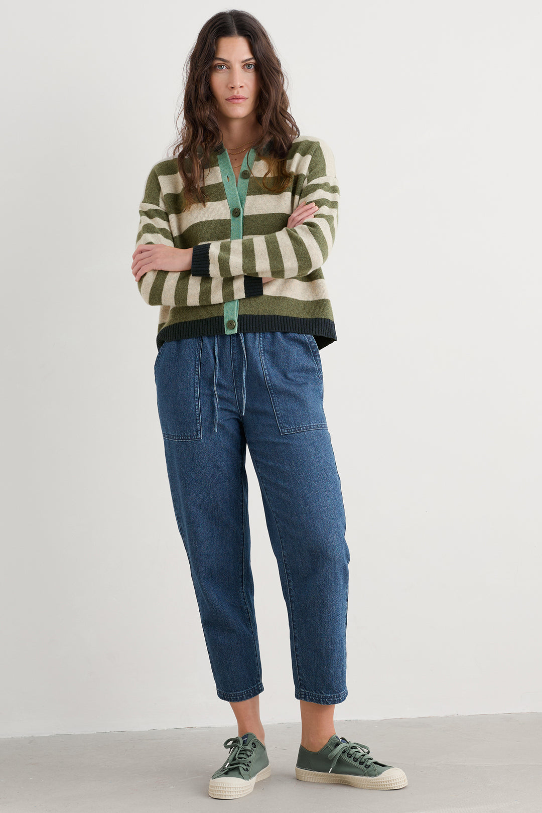 Woman wearing a striped sweater and blue jeans with green sneakers on a white background