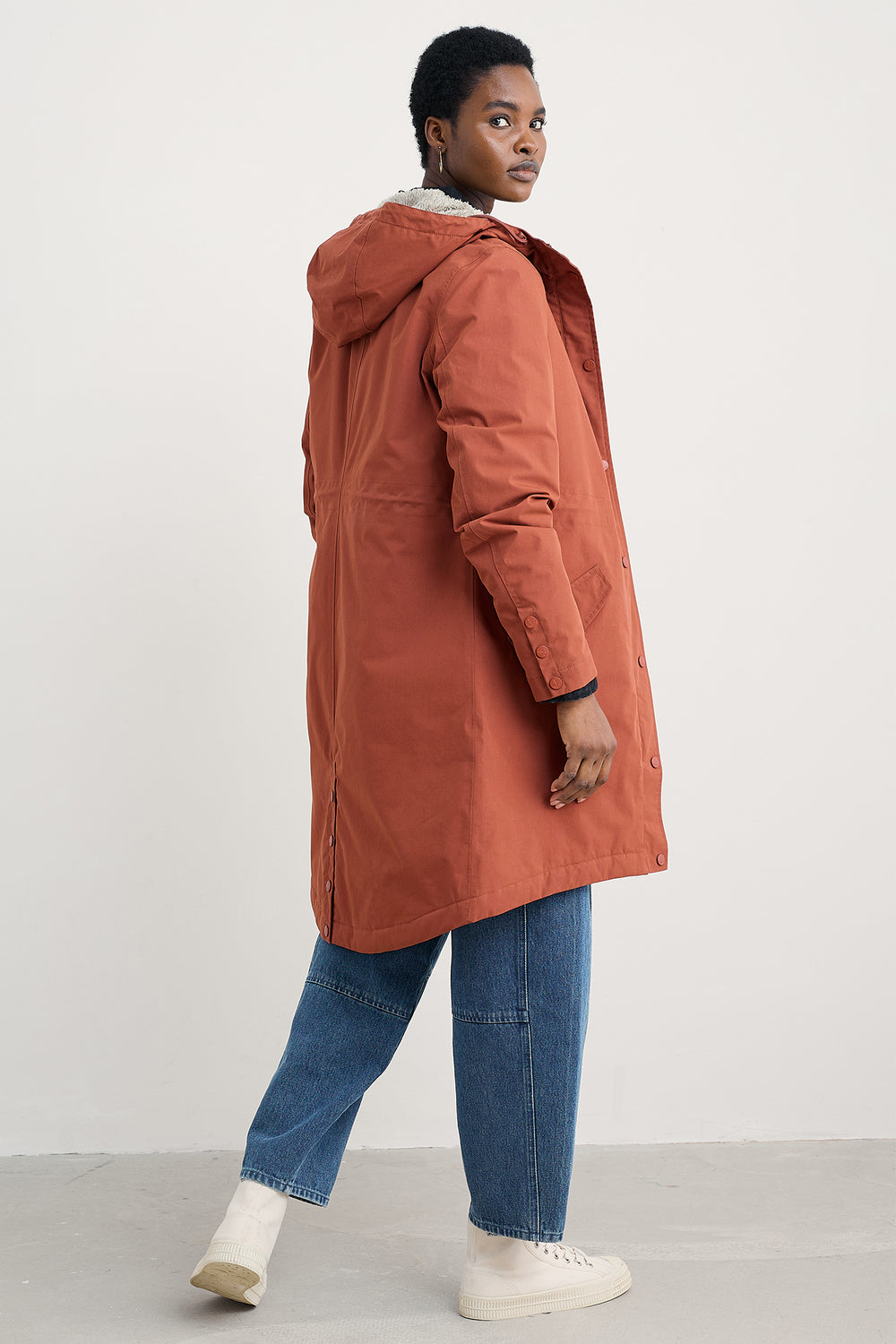 Person wearing a long rust-colored coat on a white background