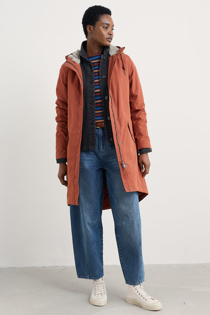 Person wearing a long orange coat over a striped sweater and blue jeans on a white background
