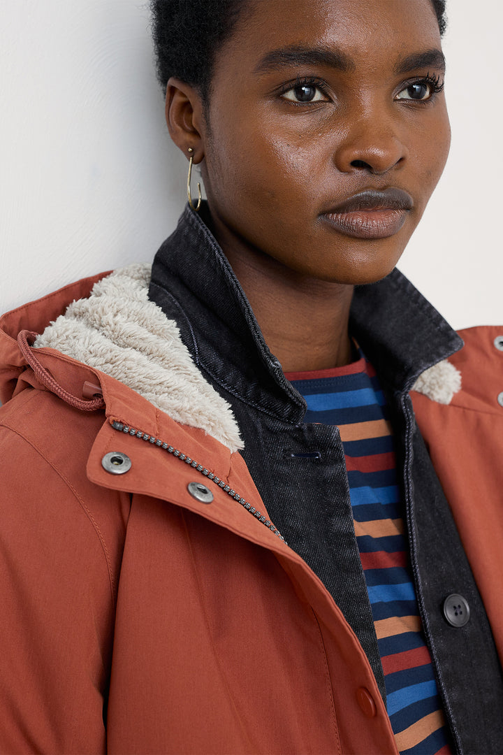 Person wearing a brown jacket with a striped shirt underneath against a white background
