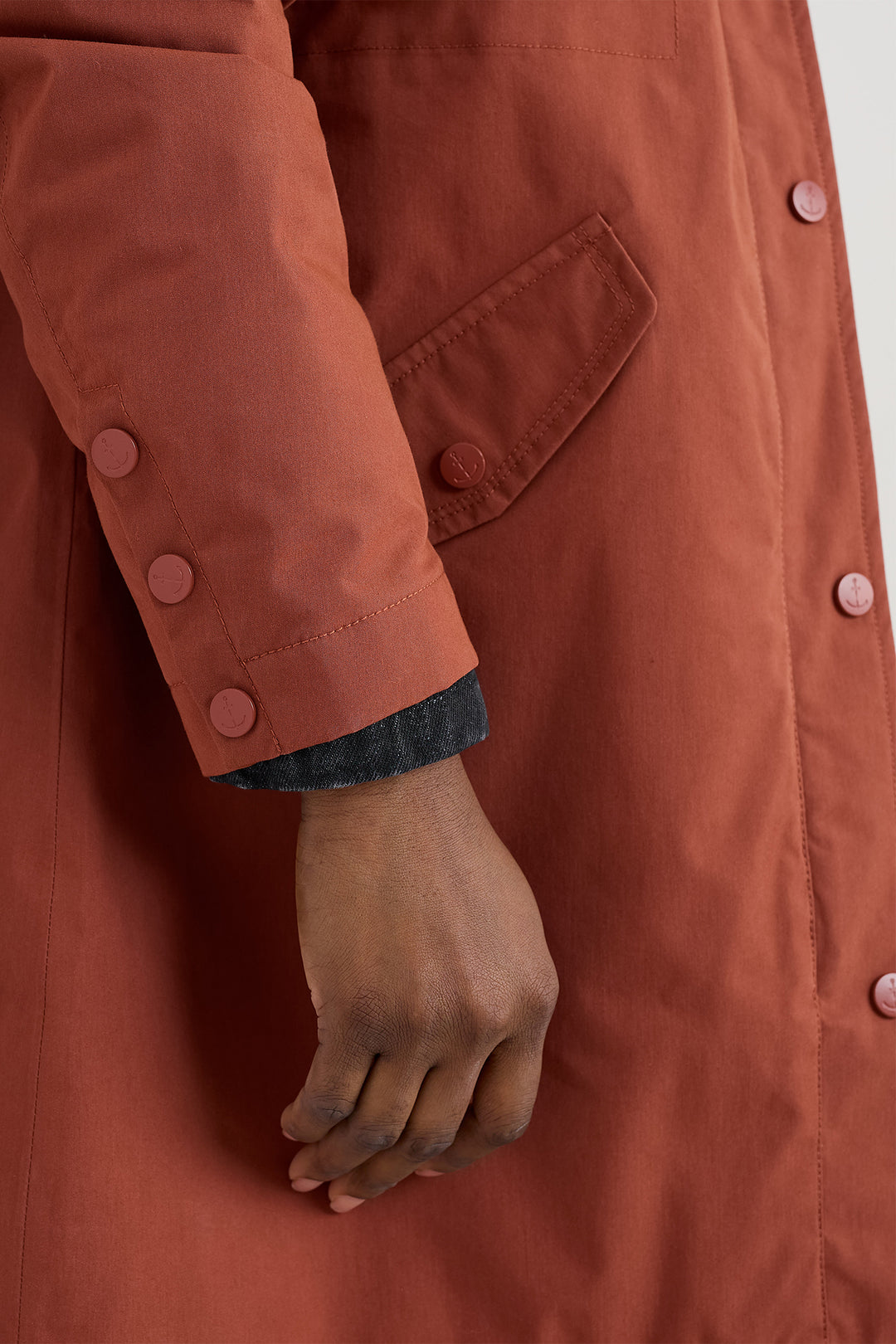 Close-up of a person wearing a brown coat with buttons, showing a hand and sleeve.