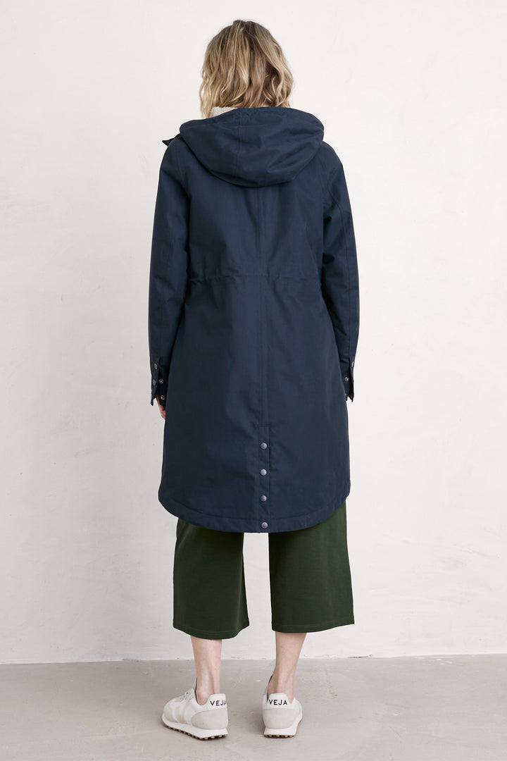 Person wearing a long navy coat with a hood on a white background