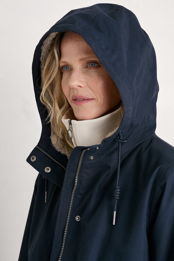 Woman wearing a navy blue hooded coat against a plain background