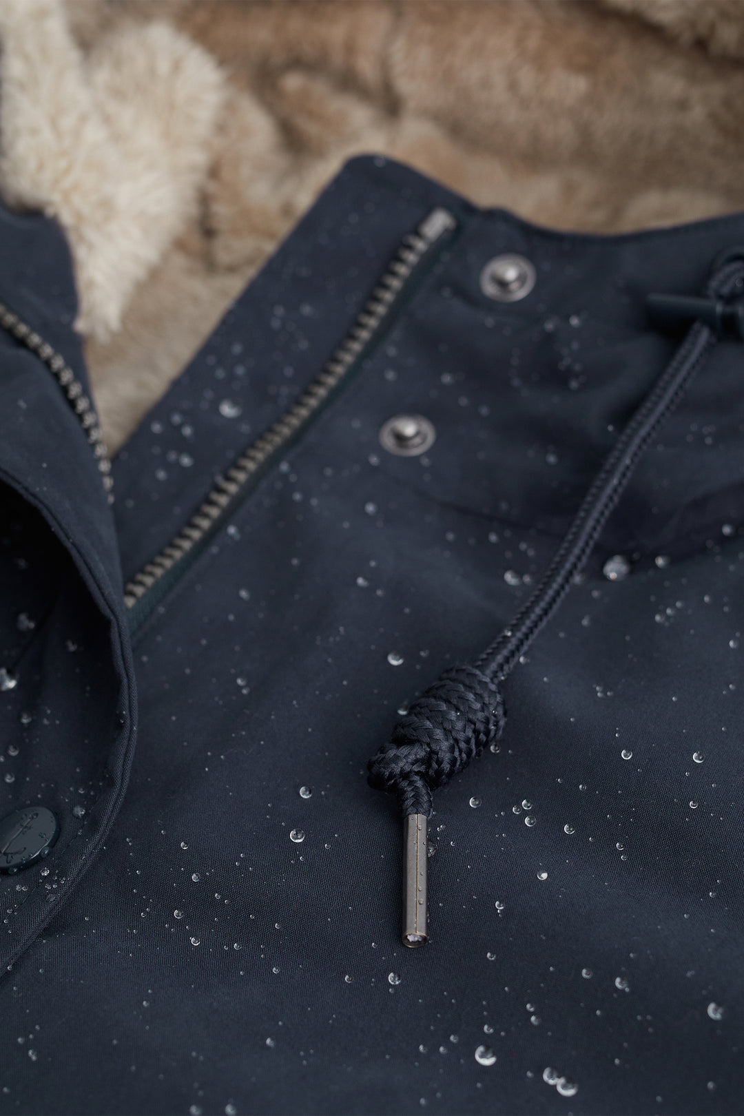 Close-up of a navy blue jacket with a drawstring and buttons on a textured beige background