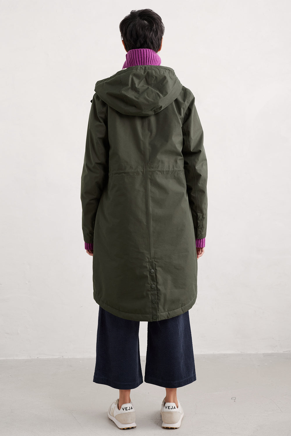 Person wearing a long green coat with a hood on a white background